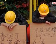 2012年12月25日，廣東中山，火炬開發(fā)區(qū)的多名建筑工人討要工作一年多的血汗錢一籌莫展，一些工人干脆將鋪蓋卷搬到了售樓部，并在門口搭起灶臺煮飯，希望以這種方式討回工錢。圖為在銷售中心門外，工人舉牌討薪。吳進/視覺中國